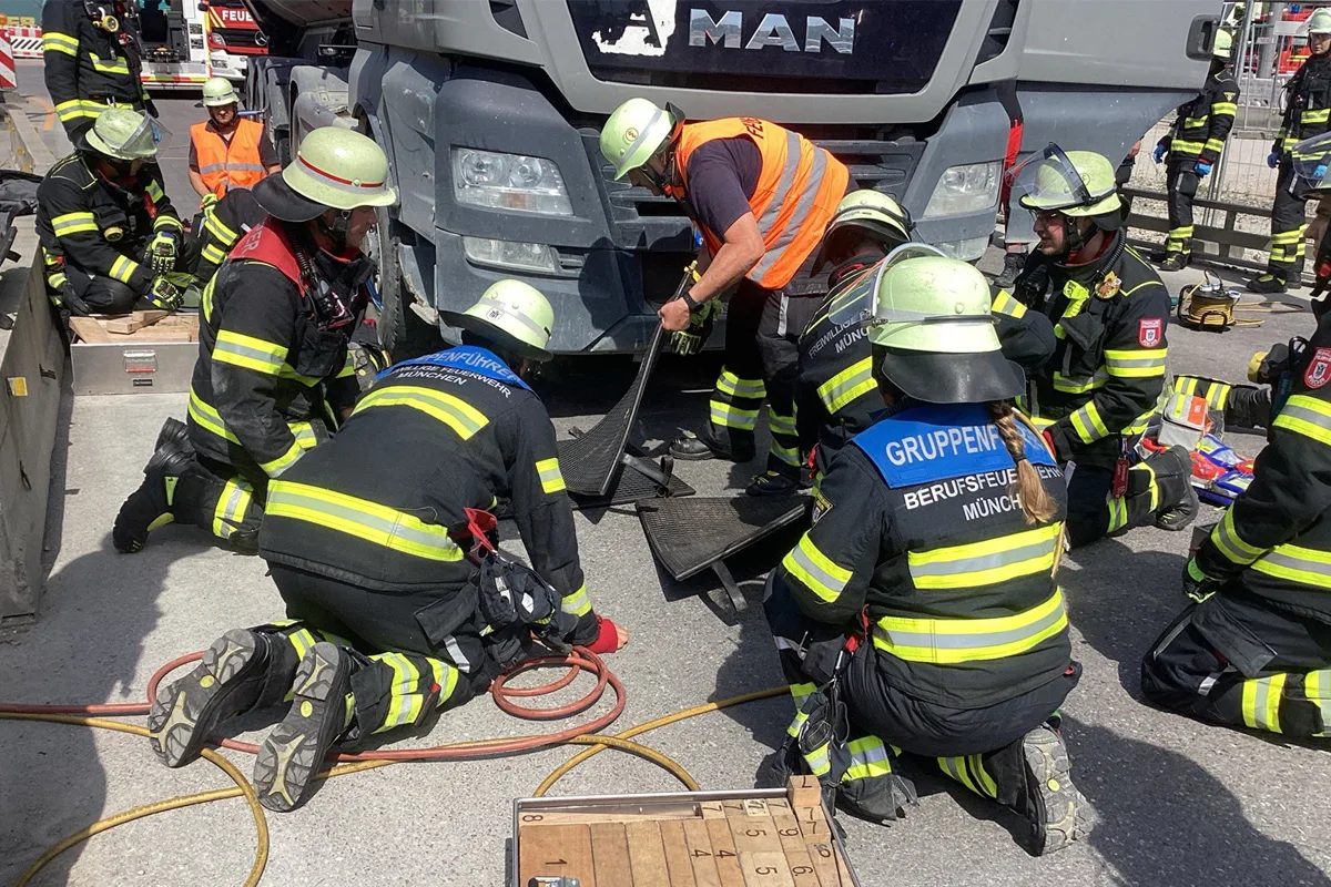 Mehrere Feuerwehrleute in Schutzkleidung arbeiten koordiniert an einem MAN-LKW, um eine Rettungsaktion durchzuführen.