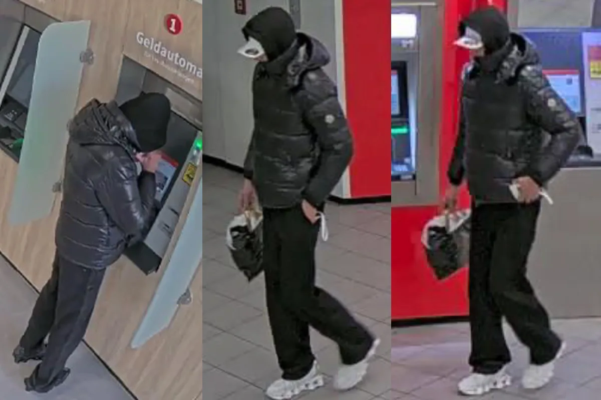 Eine vermummte Person steht an einem Geldautomaten in einer Bankfiliale. Sie trägt dunkle Kleidung und eine Gesichtsmaske.