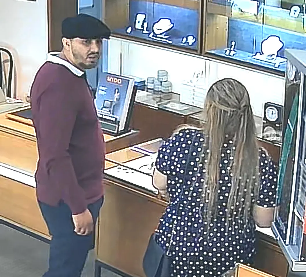 Ein Mann und eine Frau stehen in einem Juweliergeschäft. Der Mann trägt eine flache Mütze und schaut zur Kamera.