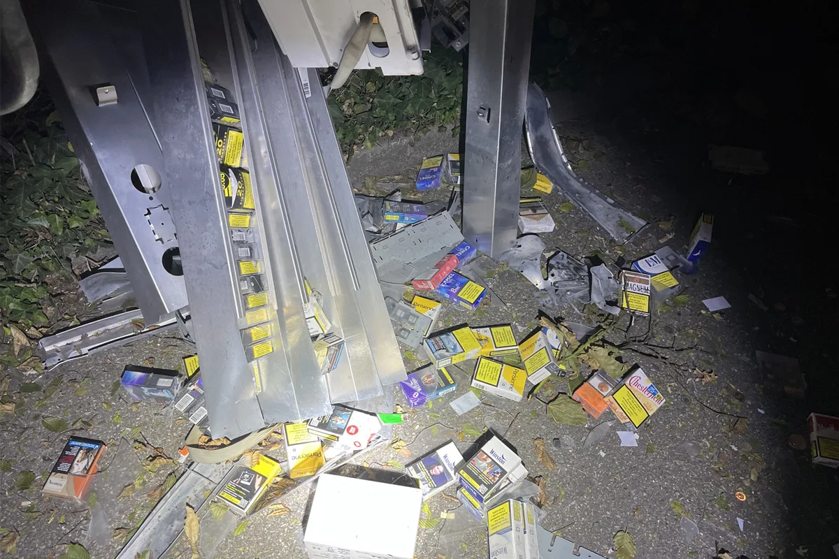 Mehrere Zigarettenschachteln und Metallteile sind auf einer Straße verstreut. Es ist Nacht, und das Bild wird mit einer Taschenlampe beleuchtet.