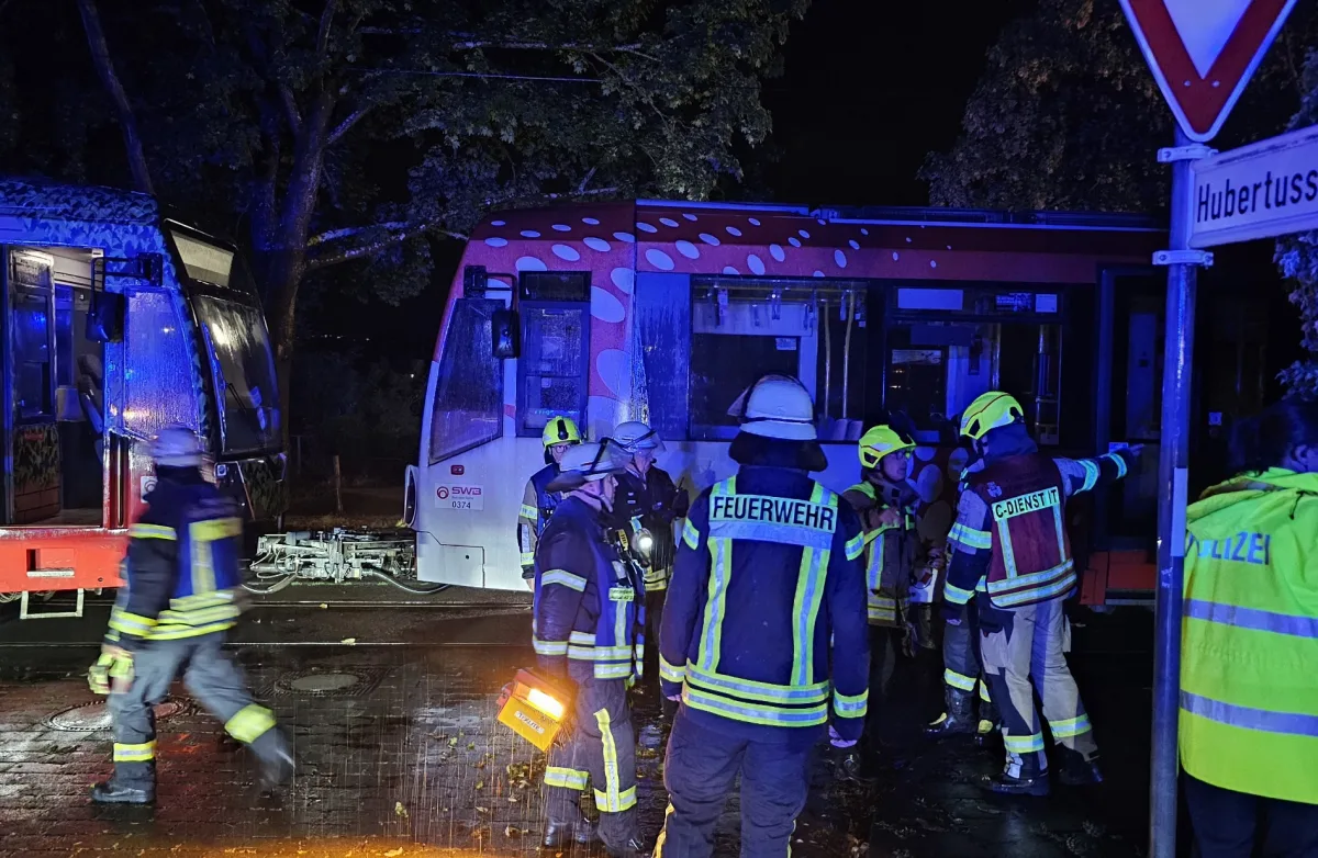 Mehrere Feuerwehrleute stehen bei Nacht vor einer Straßenbahn, die in einen Unfall verwickelt ist. Es ist dunkel und Einsatzkräfte sind im Vordergrund zu sehen.
