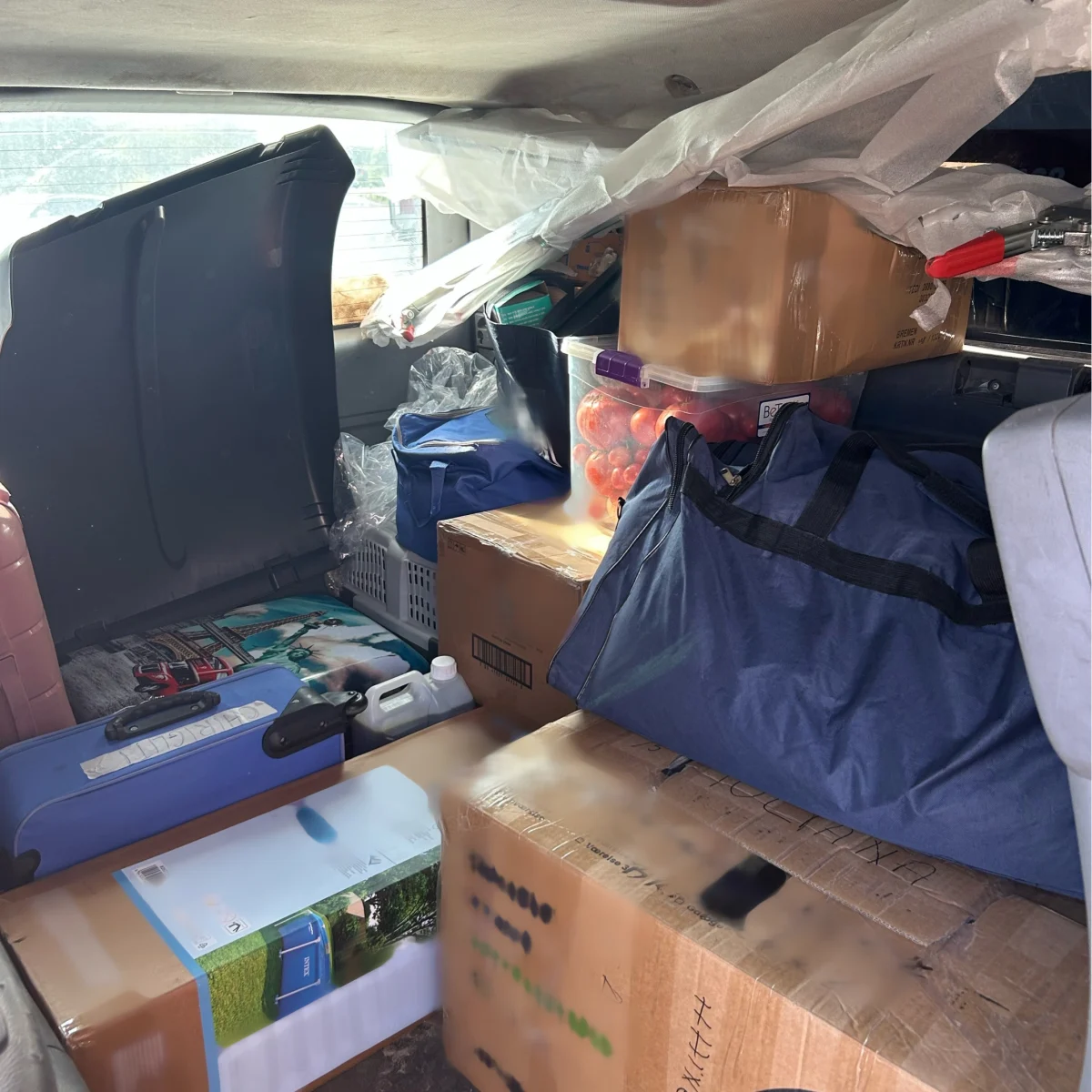 Der Innenraum eines Fahrzeugs ist überladen mit Kisten, Taschen und Plastikbehältern. Viele Gegenstände sind gestapelt und teilweise schwer erkennbar.