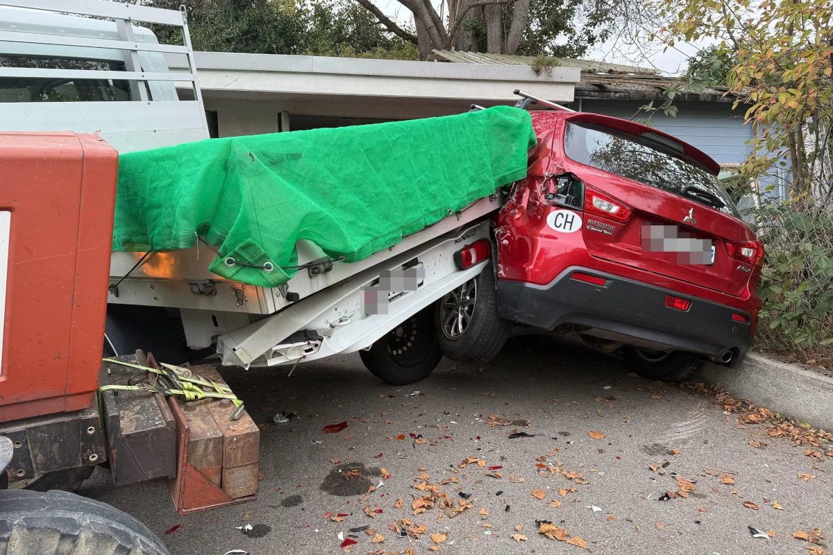 Ein roter Mitsubishi ist offensichtlich durch einen Aufprall beschädigt worden. Daneben steht ein Lastwagen mit grünem Planen über der Ladung.