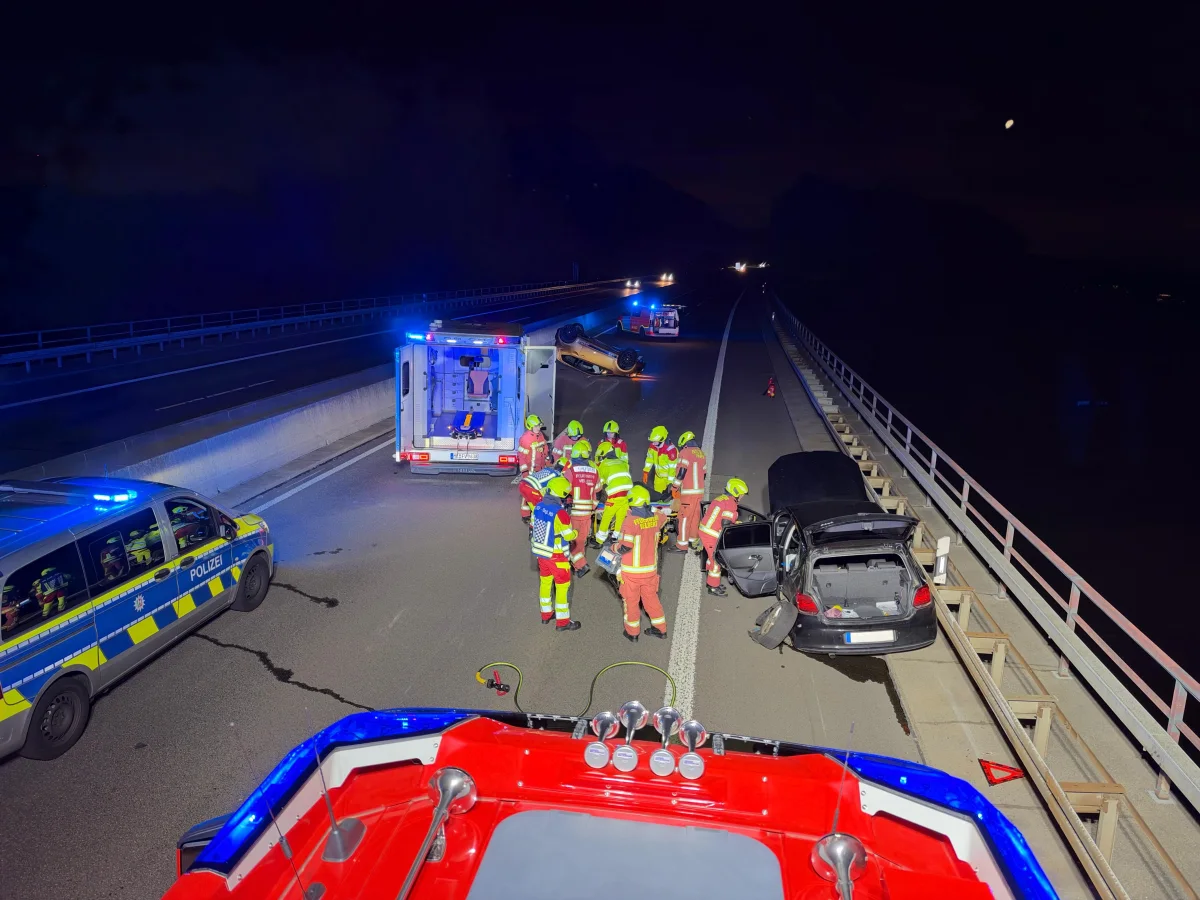 Auf einer dunklen Autobahn stehen Rettungskräfte und Polizeifahrzeuge um ein verunglücktes Auto. Blaulichter sind eingeschaltet.