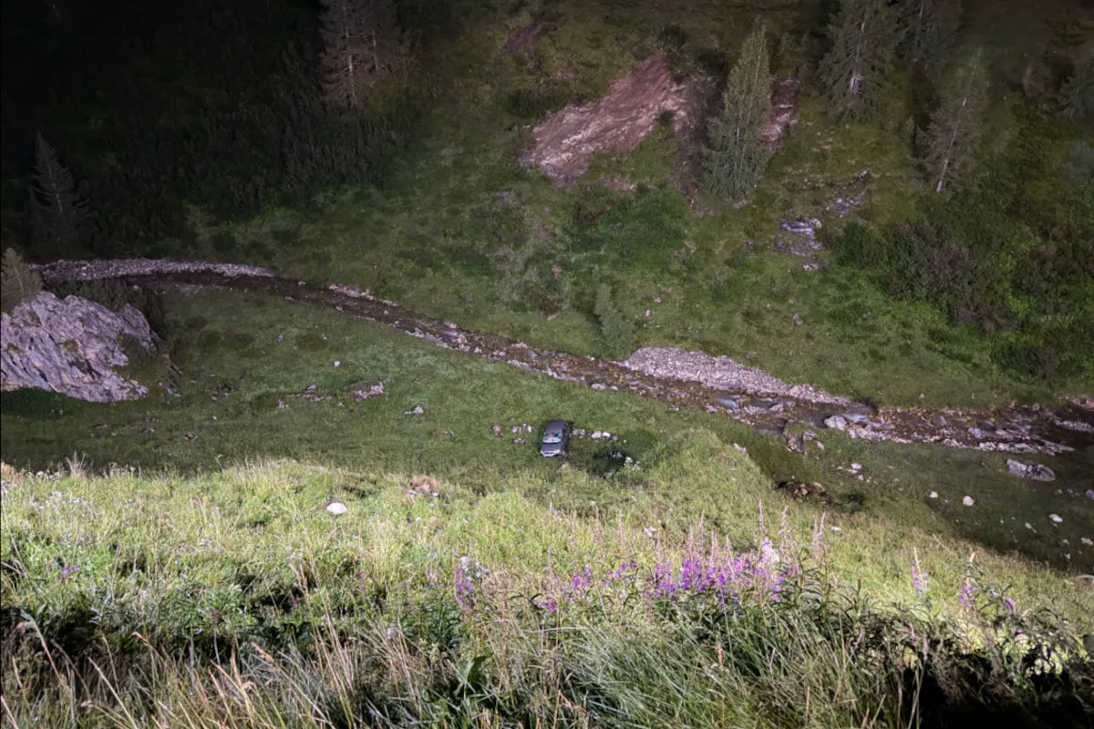 Ein einzelnes Auto ist am Grund einer steilen, begrünten Böschung neben einem kleinen Bach zu sehen. Umgeben von dichter Vegetation und Bäumen.