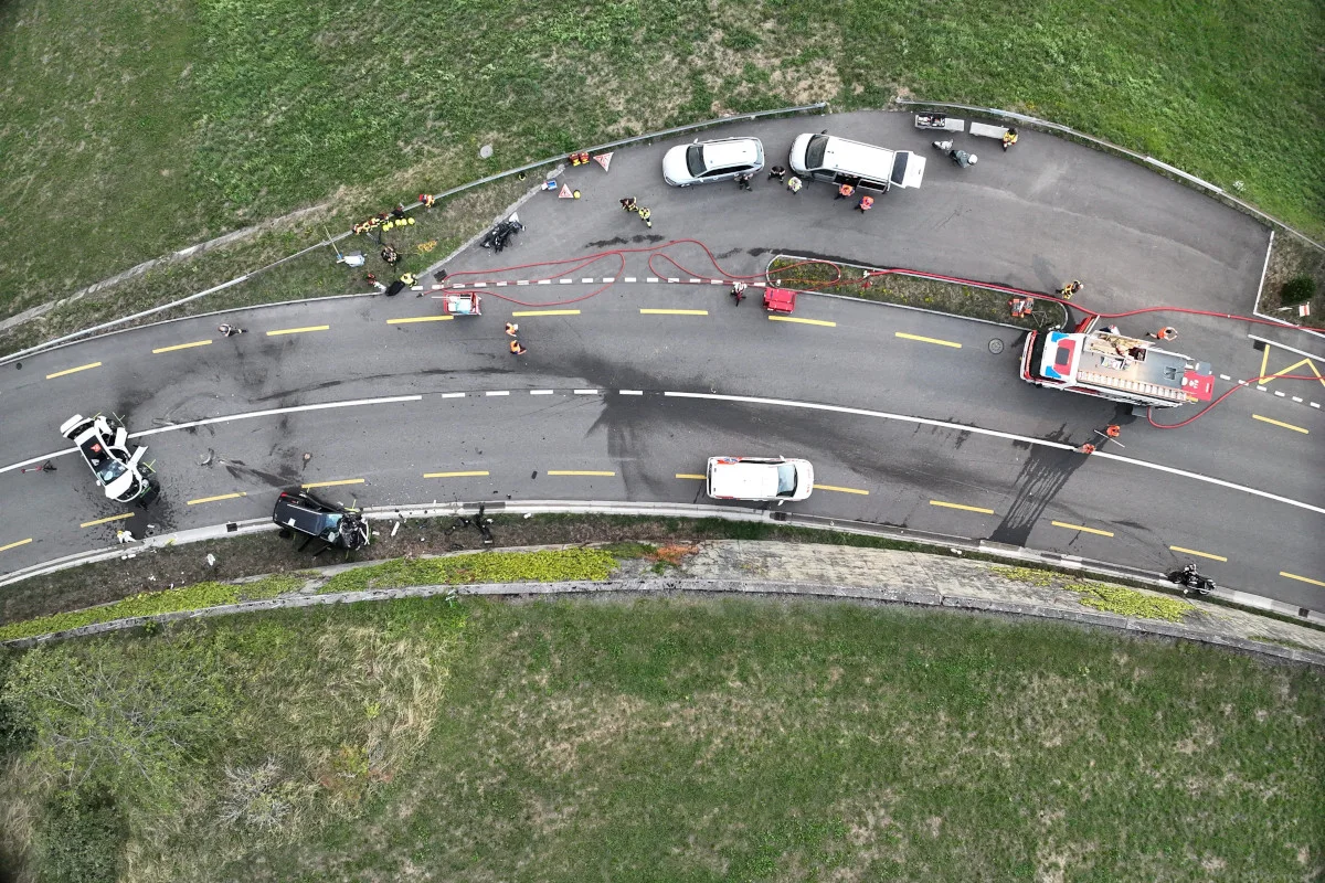Luftaufnahme zeigt mehrere Fahrzeuge und Einsatzkräfte auf einer kurvigen Landstraße nach einem Unfall.