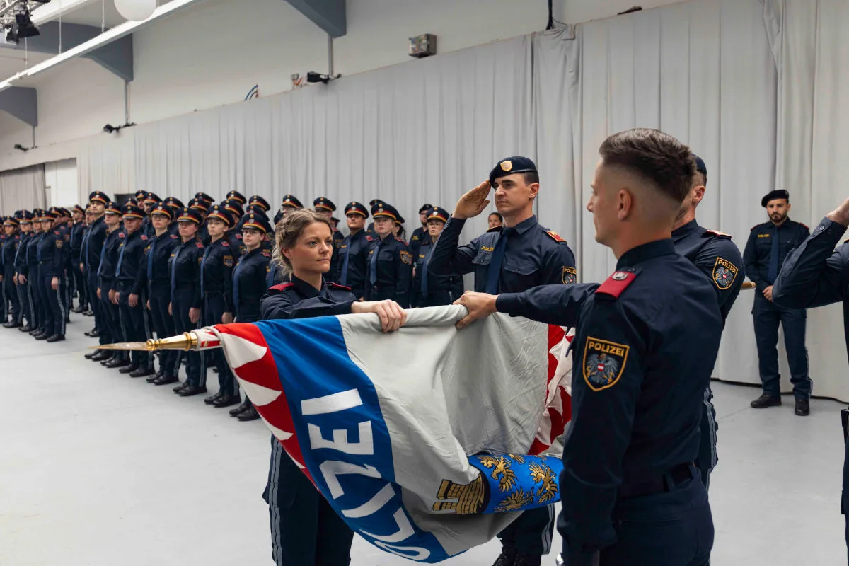 Mehrere Polizeibeamte in blauen Uniformen stehen in einem Raum. Einige halten eine Fahne und salutieren.