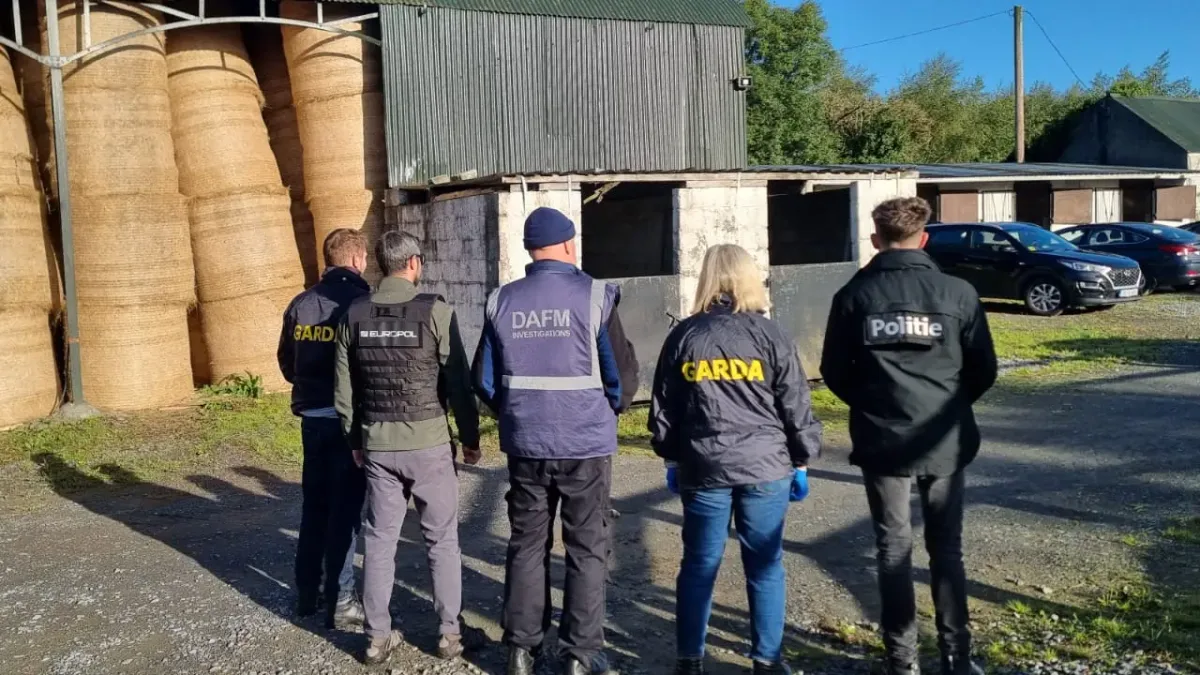Fünf Beamte verschiedener europäischer Behörden stehen mit dem Rücken zur Kamera vor einem landwirtschaftlichen Schuppen.
