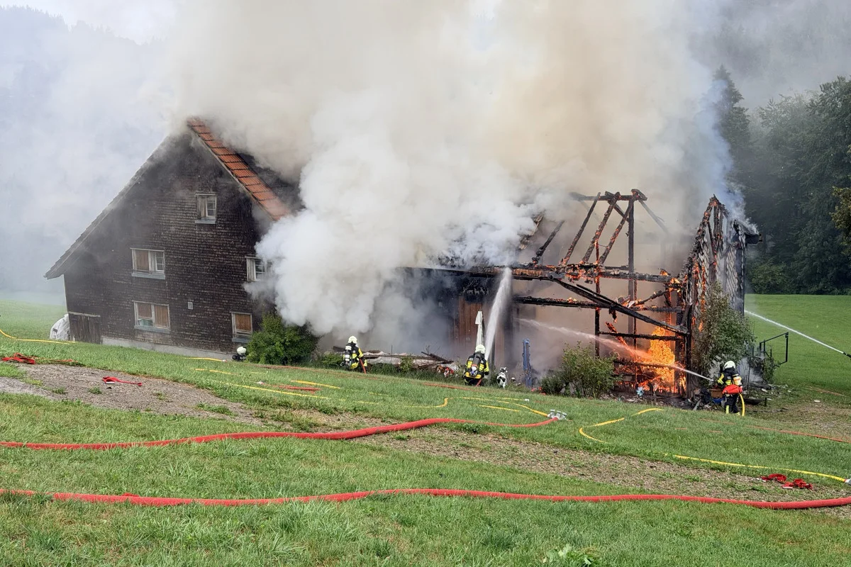 Ein ländliches Holzhaus brennt, dicker Rauch steigt auf, während Feuerwehrleute das Feuer bekämpfen.