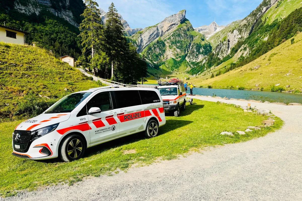 Zwei Polizeifahrzeuge der Kantonspolizei stehen auf einer grünen Wiese vor einer Bergkulisse und einem See.