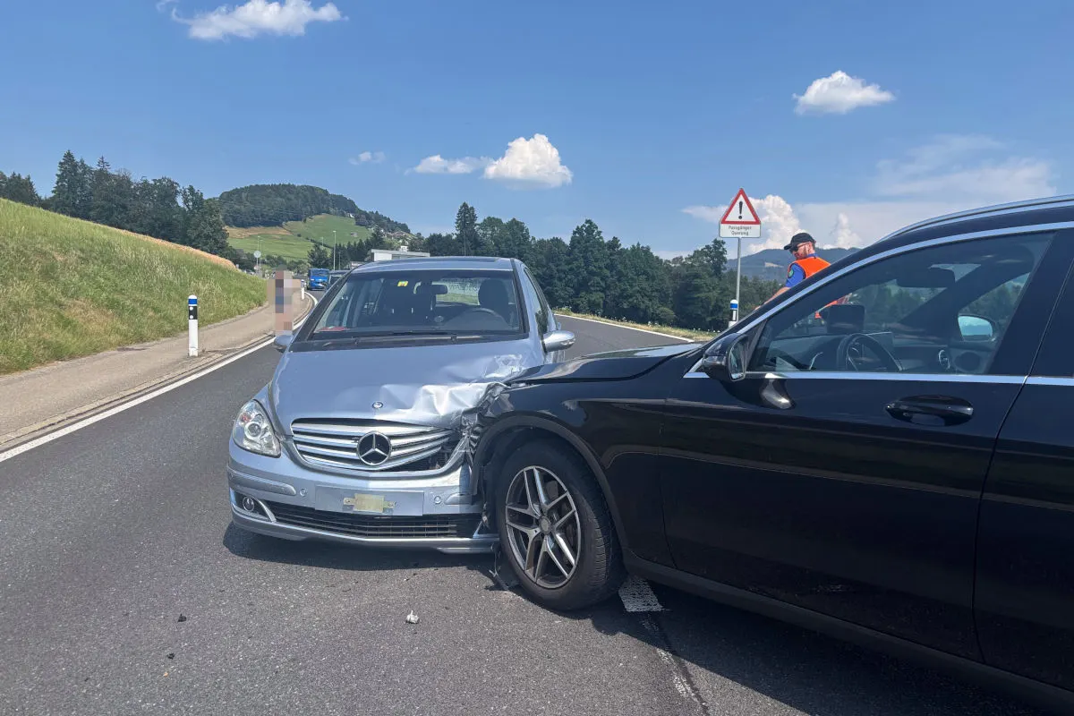 Ein silberner Mercedes und ein schwarzes Auto stehen mit Frontschäden auf einer Landstraße. Daneben steht eine Person in leuchtender Weste.