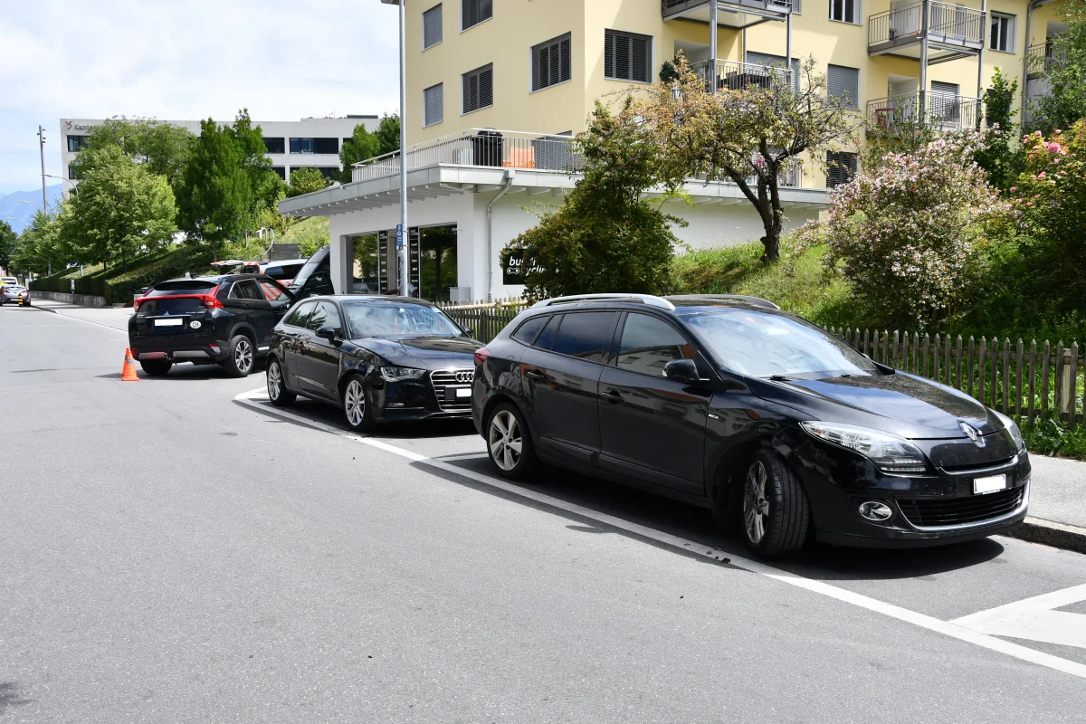 Drei schwarze Autos stehen am Straßenrand, eines davon hat sichtbare Frontschäden. Im Hintergrund sind Bäume und Gebäude zu sehen.