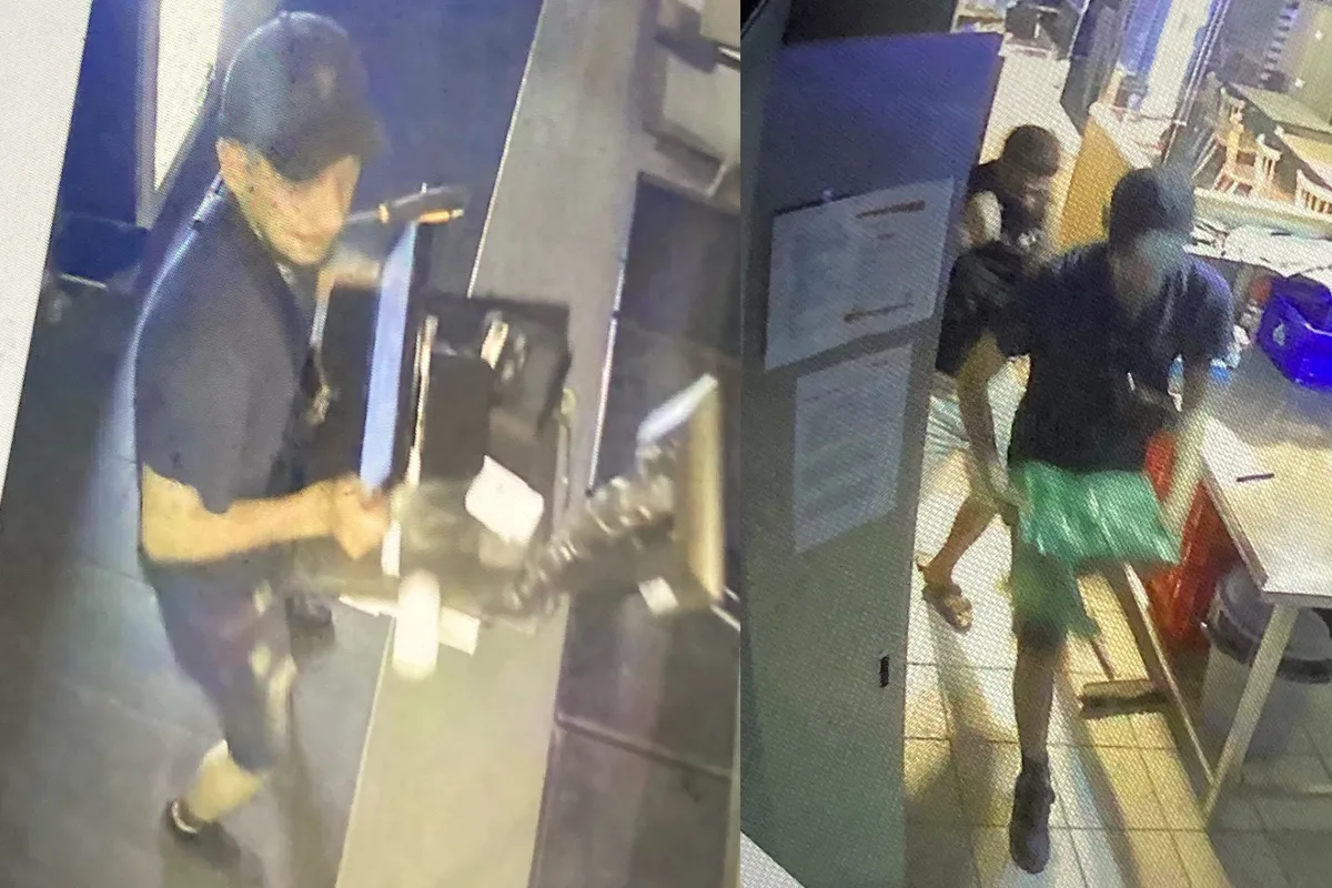Zwei Personen bewegen sich in einem Geschäft oder Büro, aufgenommen von einer Überwachungskamera. Einer trägt eine Kappe und hält ein Paket in der Hand.