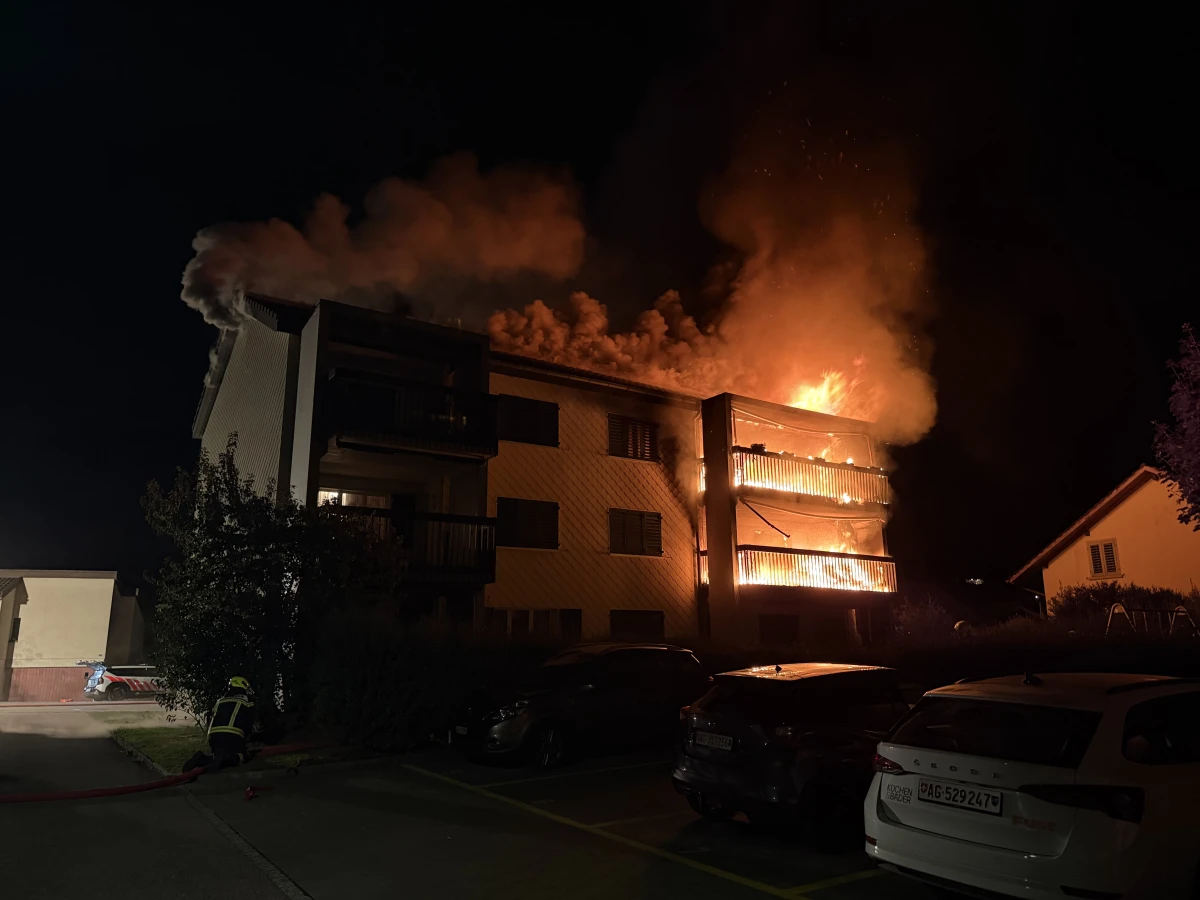 Ein mehrstöckiges Wohngebäude steht nachts in Flammen, wobei Feuerwehrleute bei der Brandbekämpfung zu sehen sind.