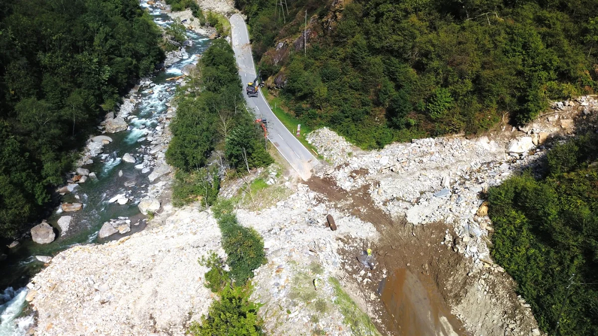 Die Luftaufnahme zeigt einen großen Erdrutsch, der eine Bergstraße blockiert, während sich ein Fluss durch die bewaldete Umgebung schlängelt.