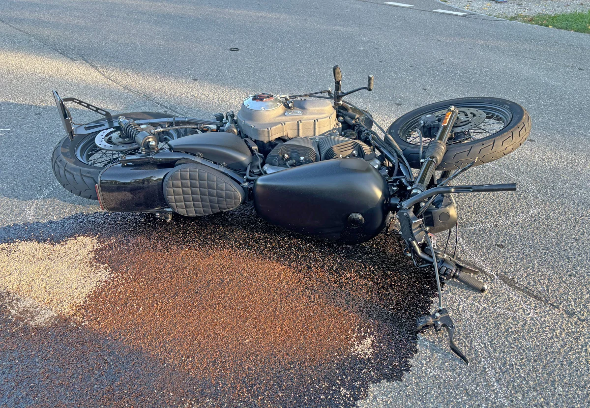 Eine schwarze Maschine liegt seitlich auf einer asphaltierten Straße. Eine dunkle Flüssigkeit hat sich daneben ausgebreitet.