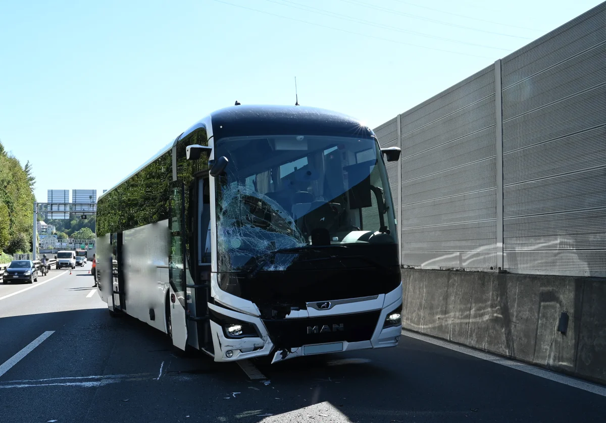 Ein Bus mit beschädigter Frontscheibe steht am rechten Fahrbahnrand einer Autobahn. Der Verkehr fließt im Hintergrund weiter.