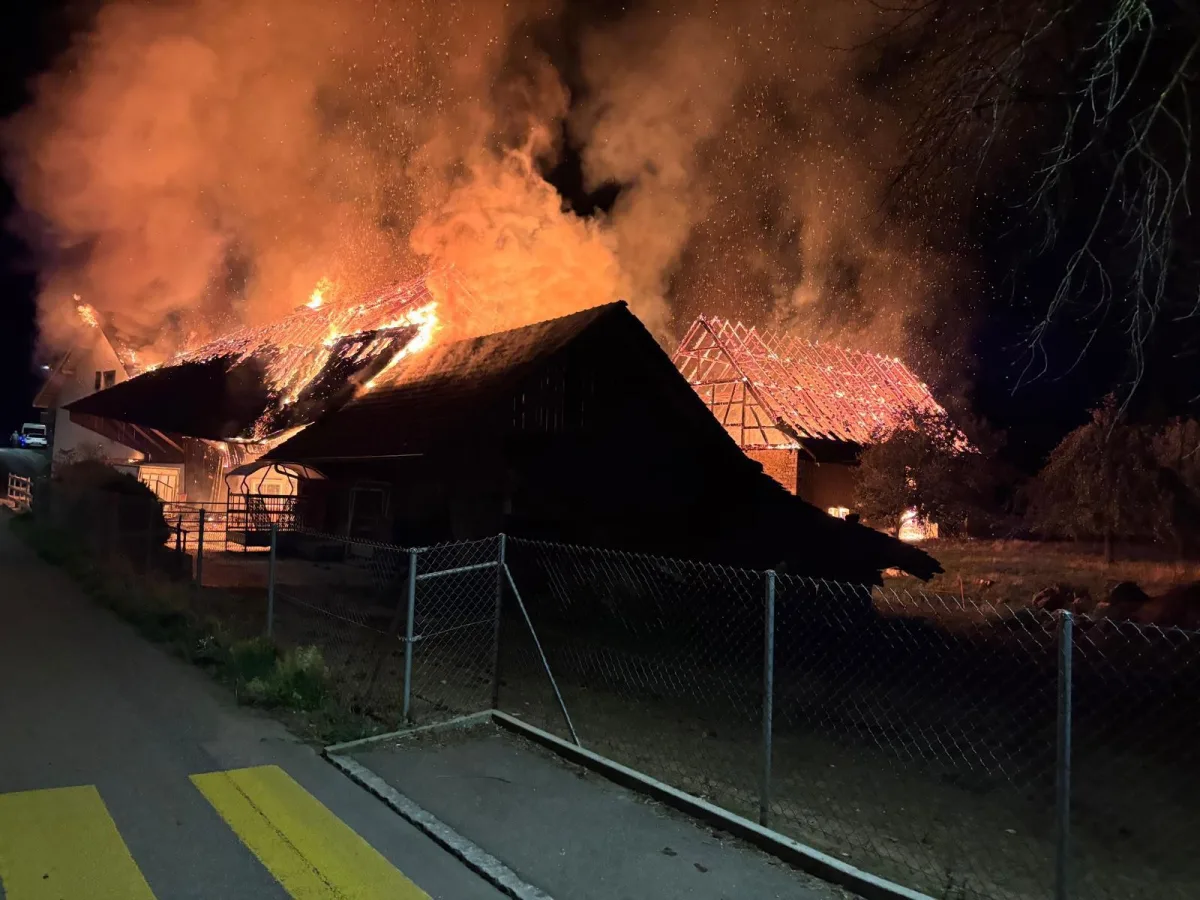 Eine große Scheune steht nachts in Flammen, umgeben von dichtem Rauch. Das Dach ist stark betroffen.