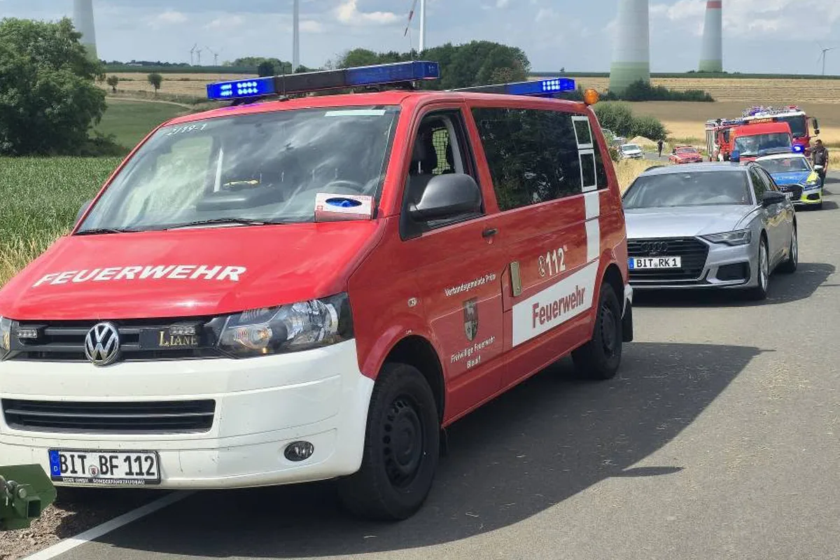 Ein rotes VW-Feuerwehrfahrzeug steht am Straßenrand in einer ländlichen Gegend, gefolgt von mehreren Einsatzfahrzeugen.