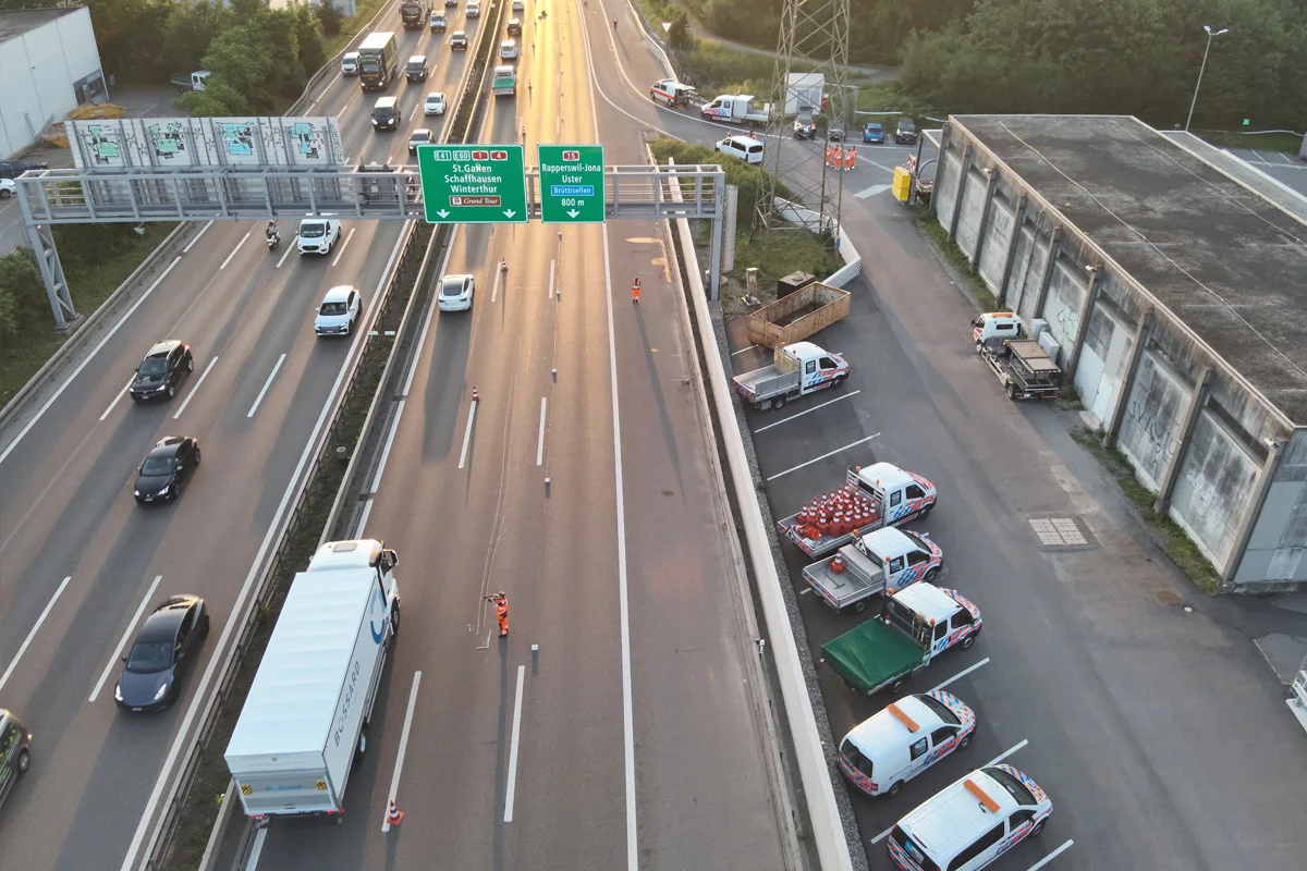 Ein gesperrter Fahrstreifen auf der Autobahn mit einem LKW und mehreren Baustellenkegeln; daneben parken Bau- und Einsatzfahrzeuge.