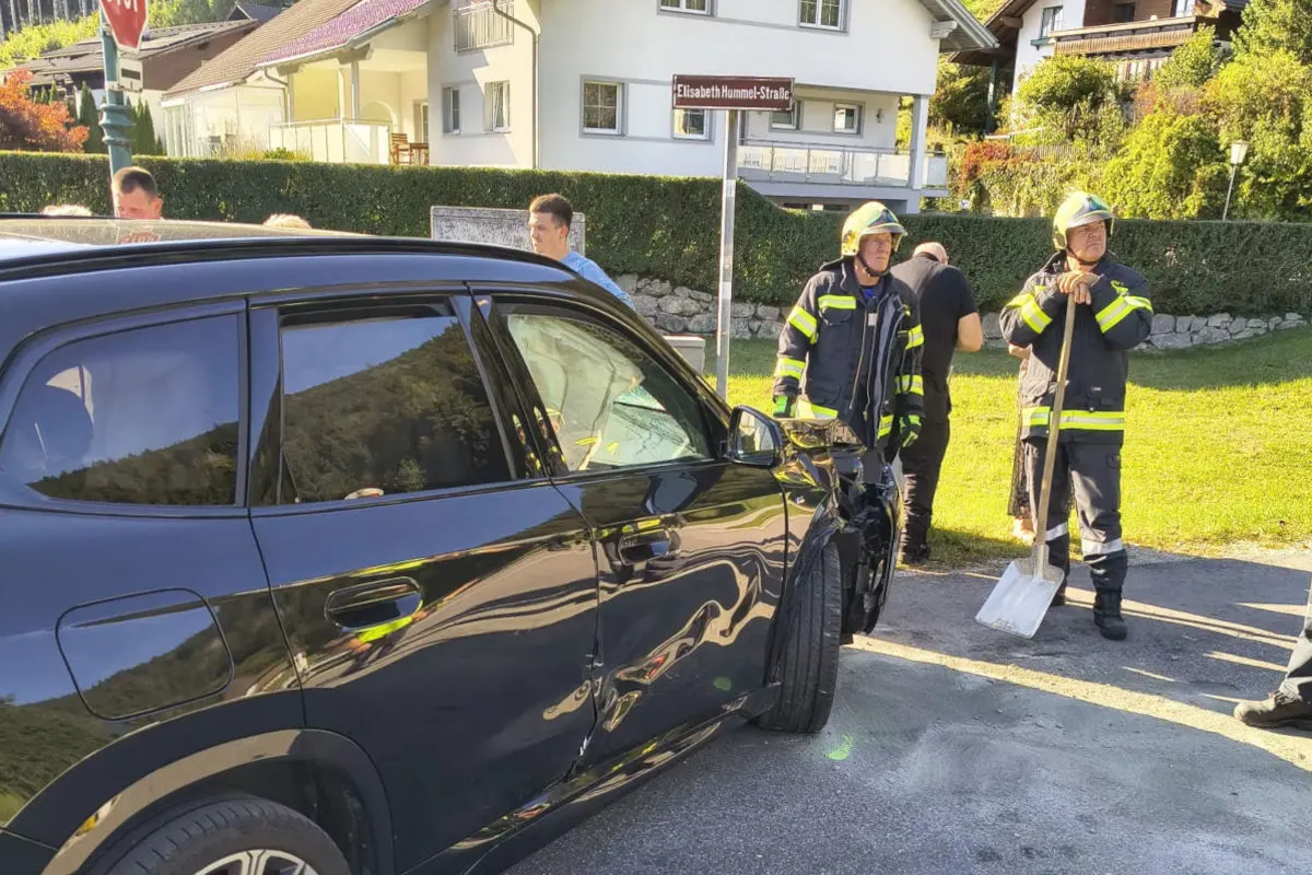 Ein Auto mit sichtbarem Schaden an der Seite steht auf einer Straße. Mehrere Feuerwehrleute in Schutzanzügen befinden sich daneben.