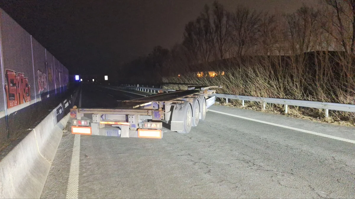 Ein leerer LKW-Anhänger steht quer auf einer Autobahnspur. Es ist Nacht, und die Szene wird durch Fahrzeuglichter beleuchtet.