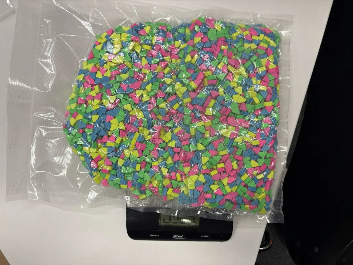 Ein vakuumverpacktes Bündel mit farbigen Tabletten liegt auf einer digitalen Waage. Die Tabletten sind blau, pink, grün und gelb.