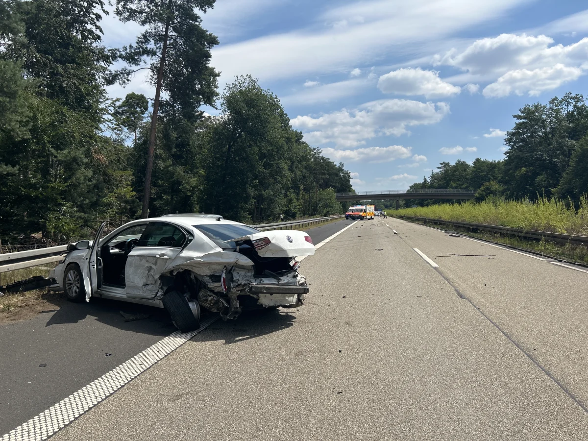 Ein weißes Auto mit erheblichen Schäden an der Rückseite steht auf einer Autobahn. Die Fahrertür ist geöffnet, Trümmer liegen verstreut.