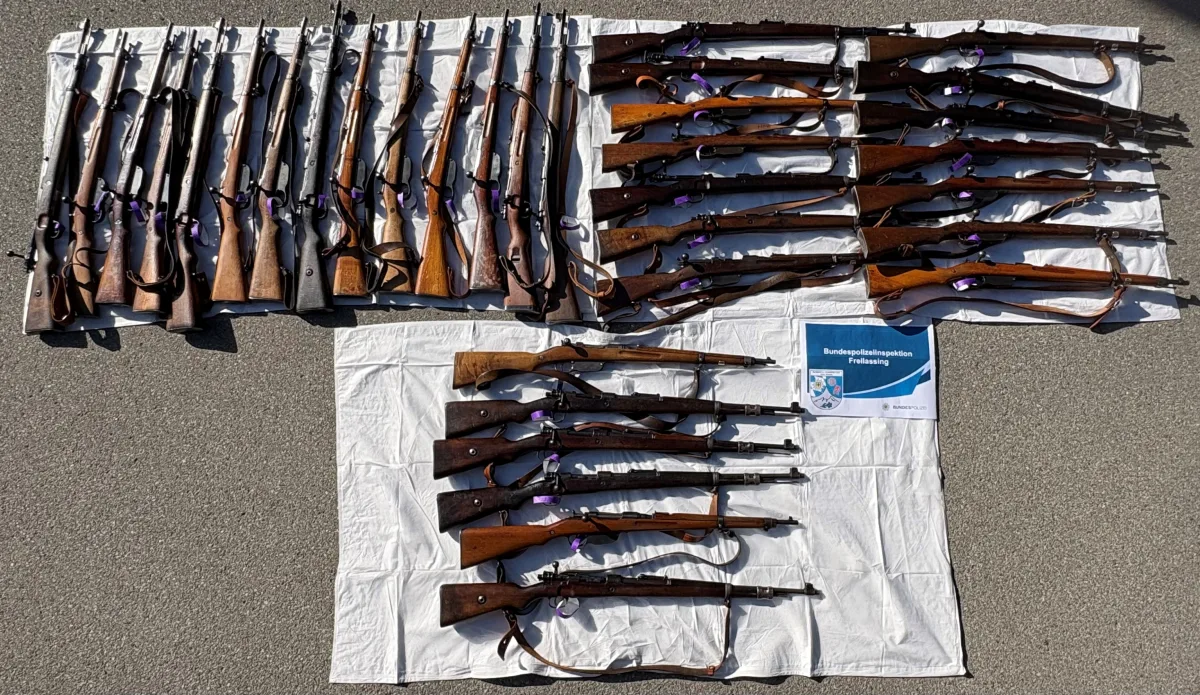 Eine Sammlung von Gewehren liegt auf weißen Tüchern ausgebreitet, begleitet von einem Schild der Bundespolizeiinspektion Freilassing.