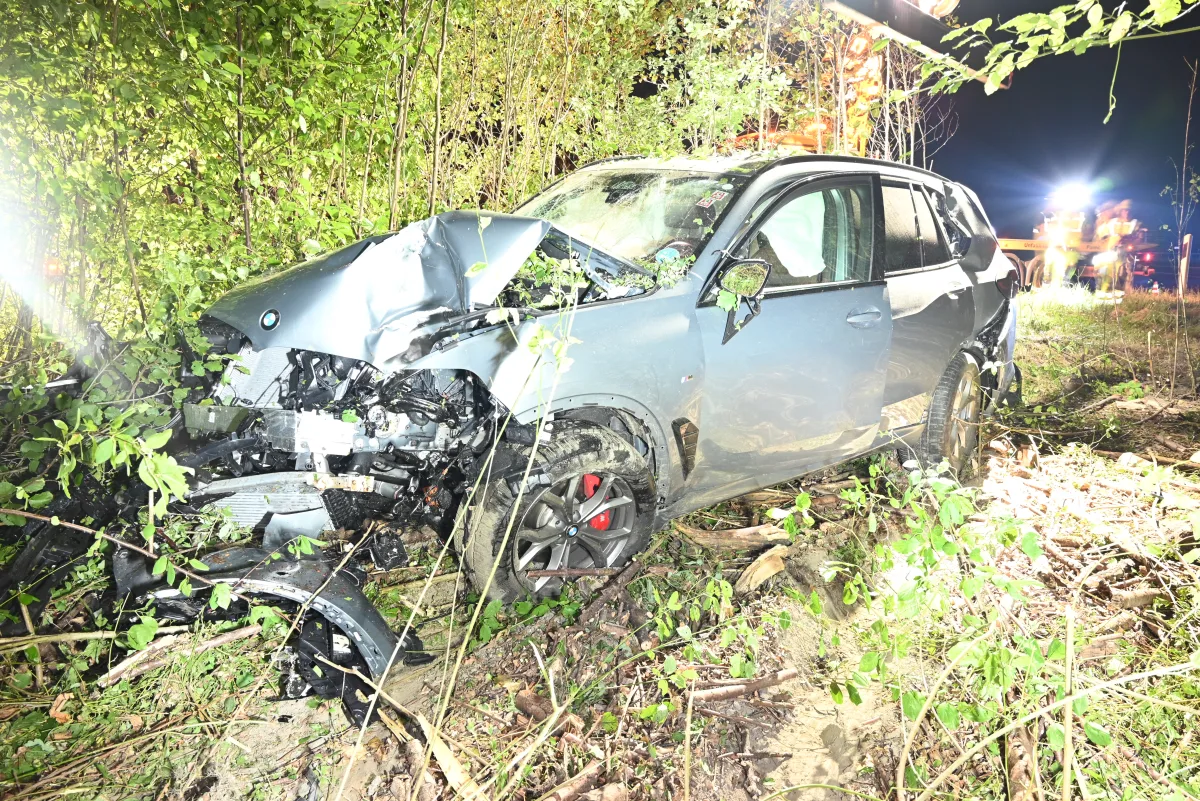Ein stark beschädigter BMW steht in einem Gebüsch. Die Front des Fahrzeugs ist stark eingedrückt, und es ist Nacht.