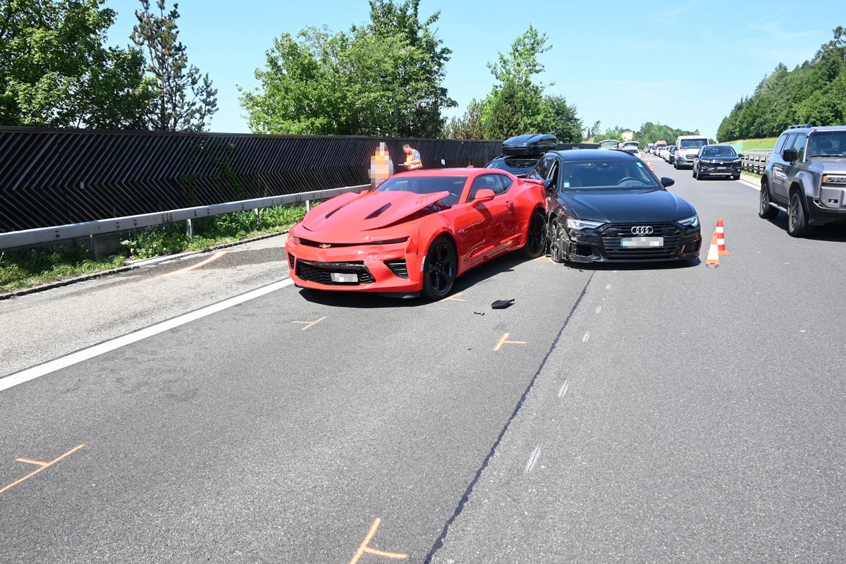 Ein rotes Auto ist mit einem schwarzen Auto auf einer Autobahn kollidiert. Beide Fahrzeuge zeigen sichtbare Schäden.