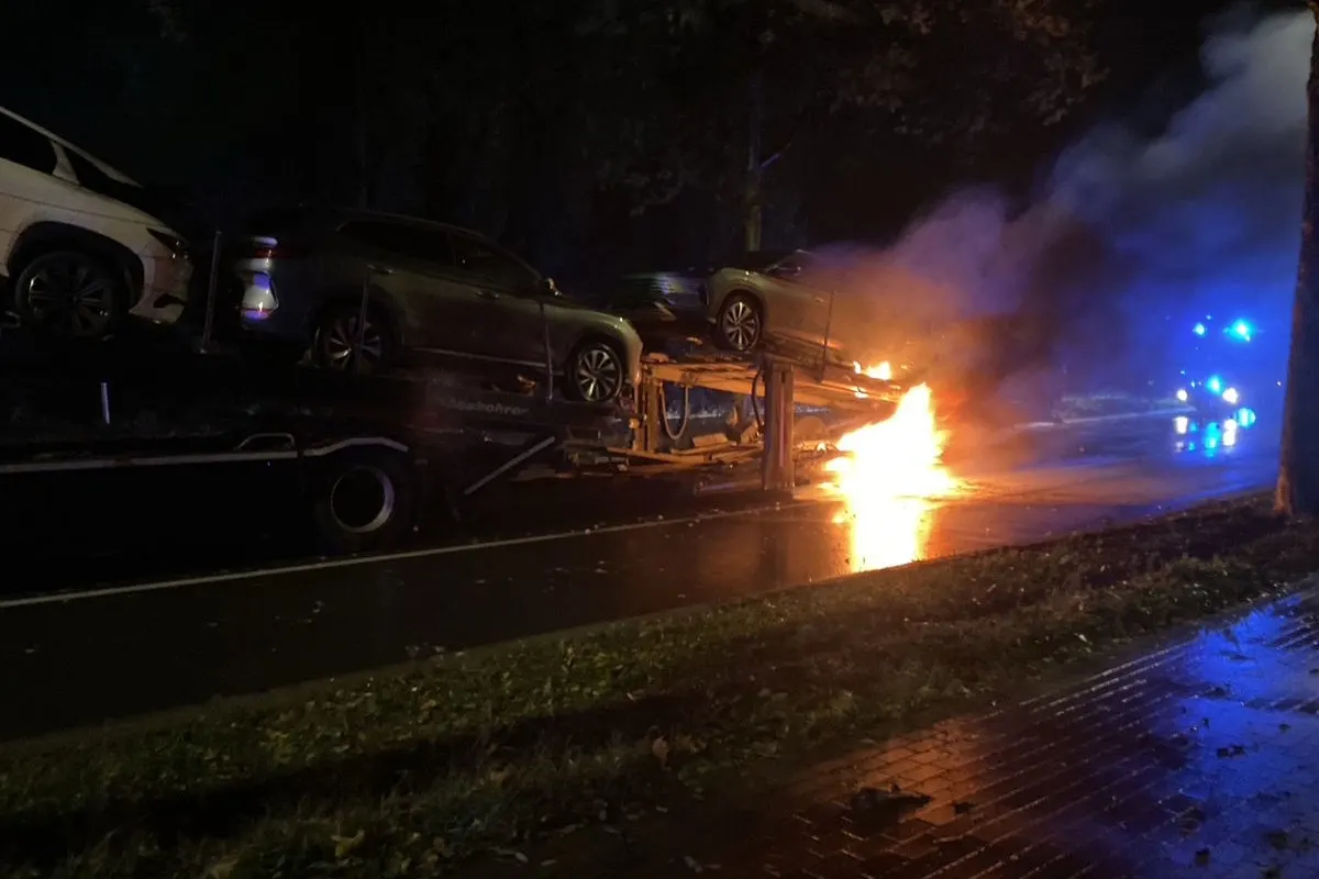 Ein Autotransporter steht bei Nacht auf einer Straße, es sind Flammen sichtbar und mehrere Autos sind auf dem Transporter geladen.