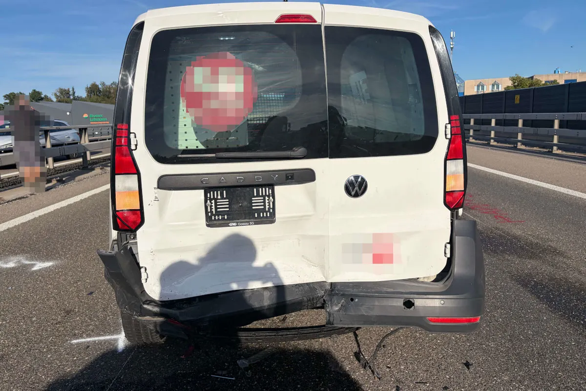 Ein weißer VW Caddy steht mit beschädigtem Heck auf einer Autobahn. Die Rückseite ist eingedrückt, und der Stoßfänger ist teilweise abgerissen.