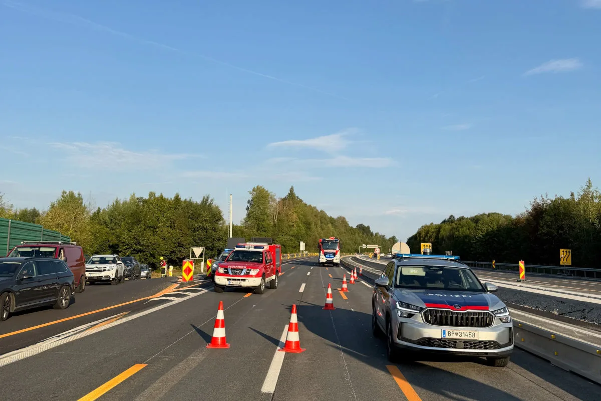 Auf einer Autobahn ist ein Einsatz mit Polizei- und Feuerwehrfahrzeugen zu sehen. Die Fahrbahn ist mit Leitkegeln abgesperrt. Im Hintergrund stehen weitere Fahrzeuge.