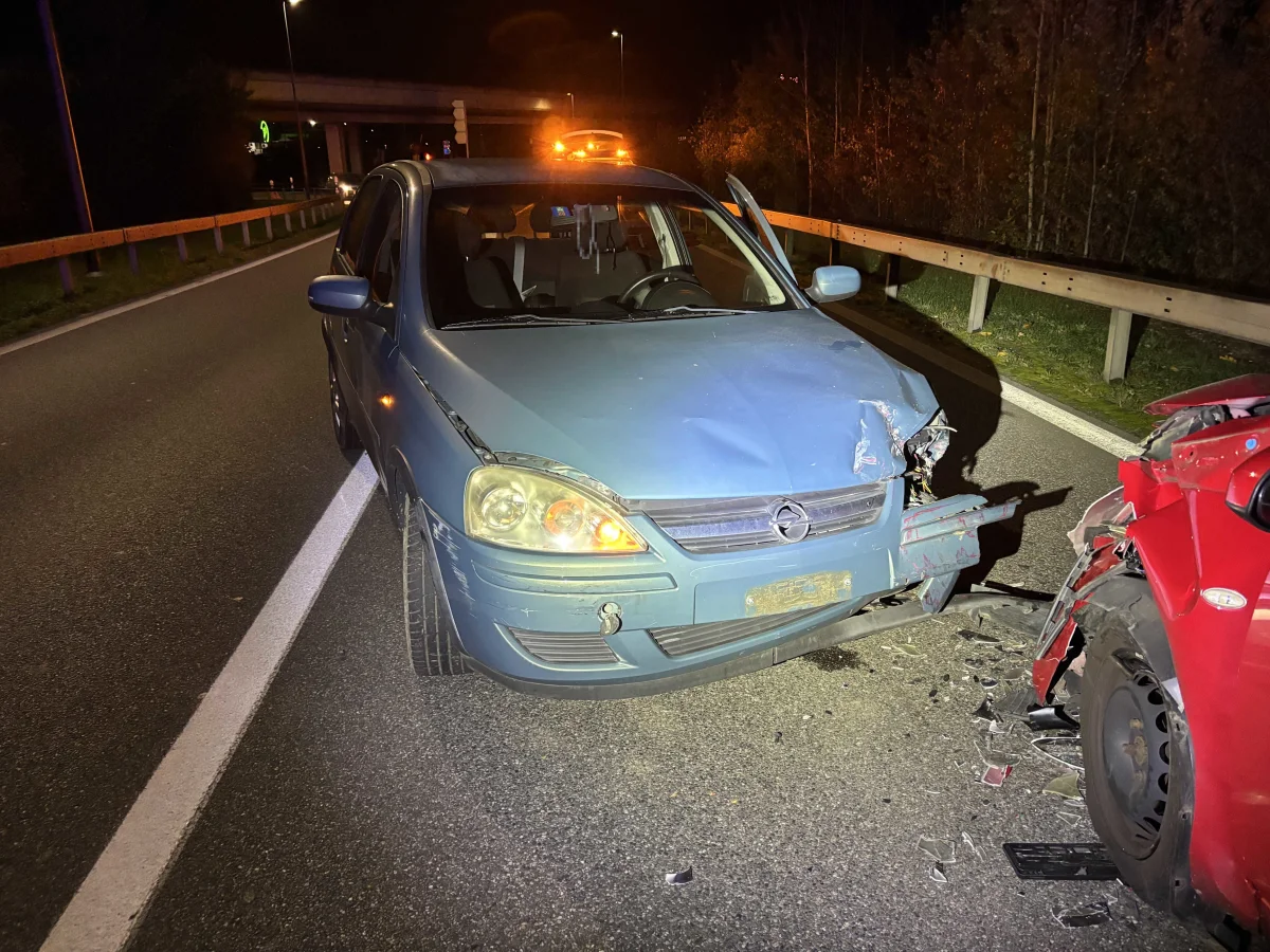 Ein blauer Opel mit beschädigter Front stößt bei Nacht mit einem roten Auto auf einer Landstraße zusammen. Trümmerteile liegen verstreut.