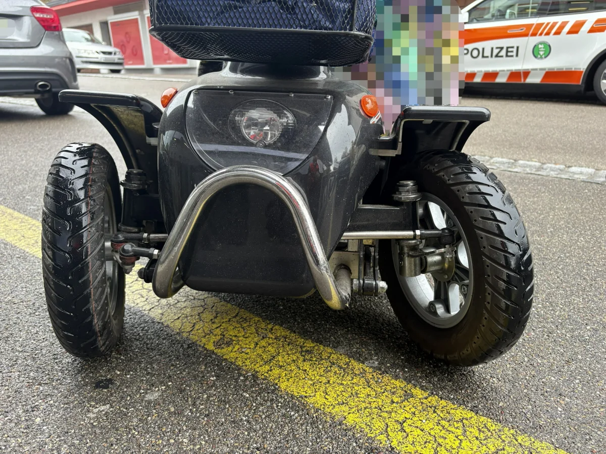 Ein schwarzes Elektromobil steht auf einer Straße, während im Hintergrund ein Polizeifahrzeug zu sehen ist.