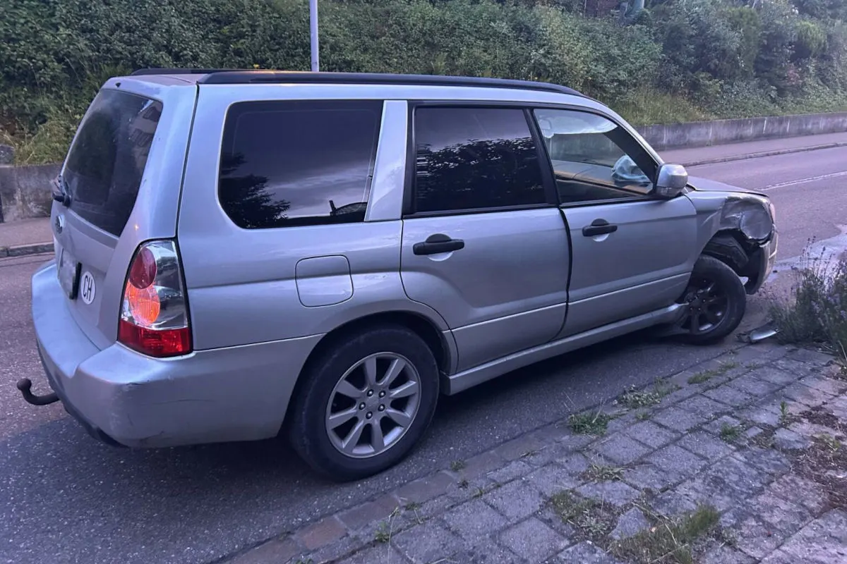 Ein silberner SUV parkt am Straßenrand mit deutlich sichtbaren Schäden an der Vorderrad-Kotflügel und Fahrzeugfront.
