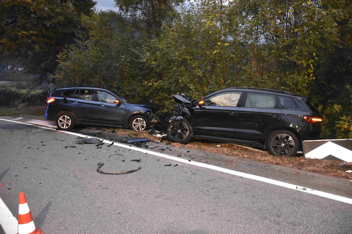 Zwei Fahrzeuge stehen beschädigt an einem Straßenrand, nach einem Frontalzusammenstoß. Autoteile sind auf der Fahrbahn verstreut.