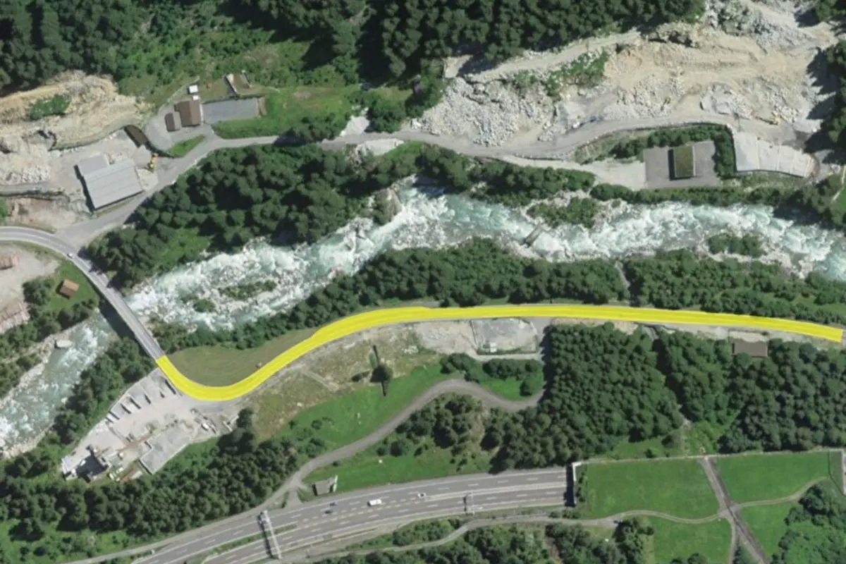 Das Bild zeigt eine kurvenreiche Landstraße neben einem fließenden Fluss, umgeben von dichtem Grün und felsigen Abhängen in einer bergigen Region.