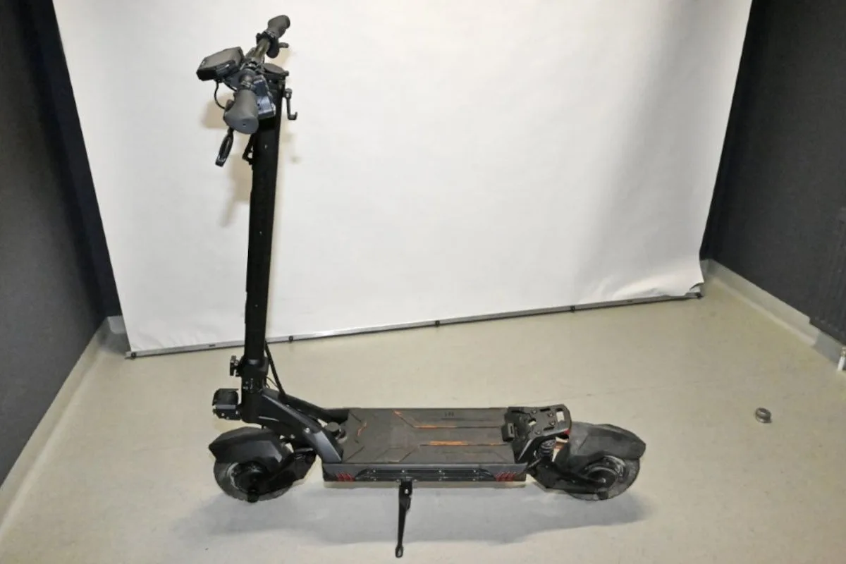 Ein schwarzer E-Scooter steht in einem neutralen Raum mit hellem Boden und einem weißen Fotohintergrund.