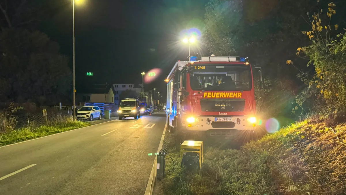 Ein rotes Feuerwehrfahrzeug steht bei Nacht mit eingeschaltetem Blaulicht am Rand einer Landstraße. Im Hintergrund sind weitere Fahrzeuge zu sehen.
