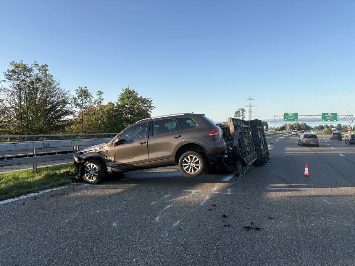 Ein brauner SUV liegt schräg auf einem umgestürzten Anhänger auf der Autobahn. Mehrere Fahrzeuge sind im Hintergrund zu sehen.