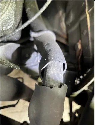 Nahaufnahme eines beschädigten Kabels im Motorraum eines Fahrzeugs. Das Kabel zeigt sichtbare Abnutzungen und mögliche Hitzeschäden.