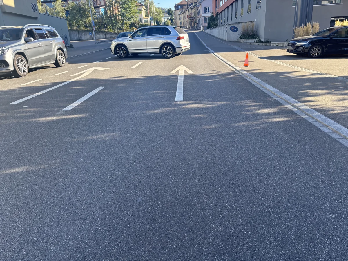 Eine Kreuzung in einem Wohngebiet mit einem Verkehrskegel auf einer leeren Fahrspur. Drei Fahrzeuge stehen auf der Straße.