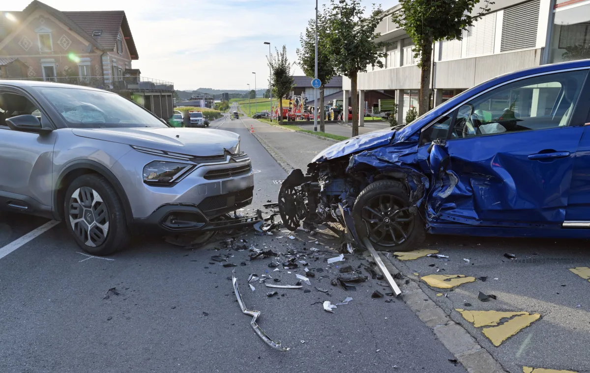 Zwei Autos, ein silbernes und ein blaues, sind frontal auf einer Straßeneinfahrt zusammengestoßen, mit sichtbaren Blechschäden und Trümmern auf der Straße.