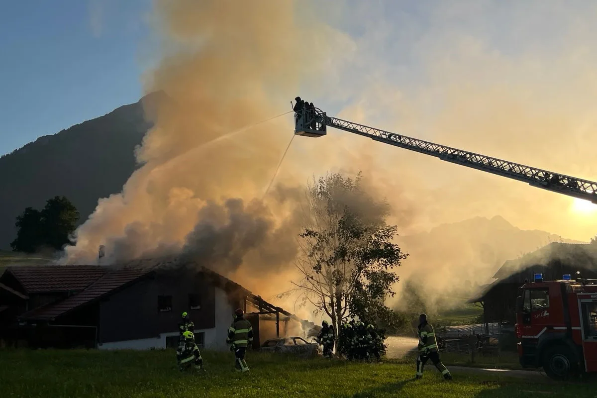 Mehrere Feuerwehrmänner sind im Einsatz, um ein brennendes Gebäude mit einem Wasserwerfer zu löschen. Eine Drehleiter wird zur Bekämpfung des Feuers eingesetzt, während dichter Rauch aufsteigt.