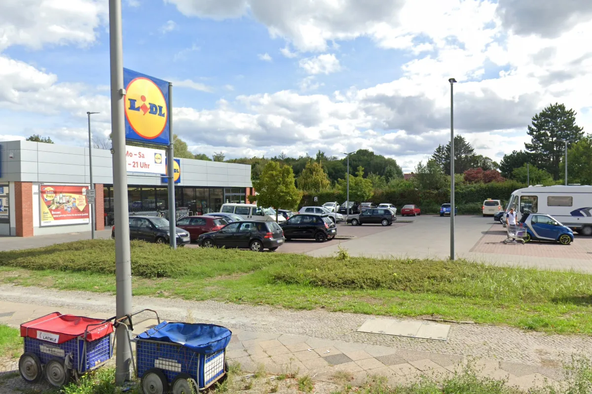 Auf dem Lidl-Parkplatz sind mehrere geparkte Autos und ein Wohnmobil zu sehen. Im Vordergrund stehen zwei Einkaufswagen.