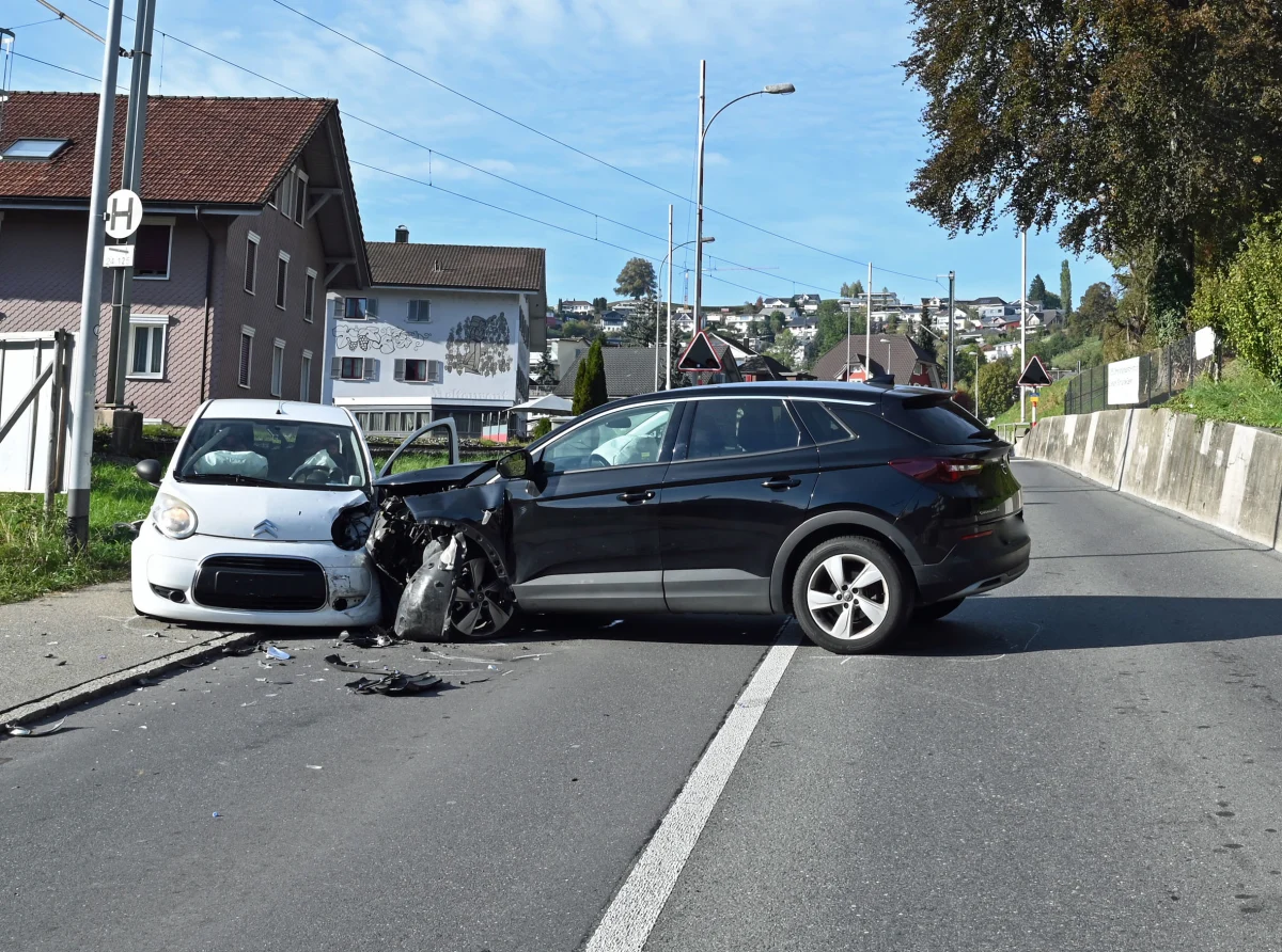Ein weißer Citroën und ein schwarzes Auto sind frontal auf einer Straße kollidiert. Beide Fahrzeuge sind stark beschädigt.