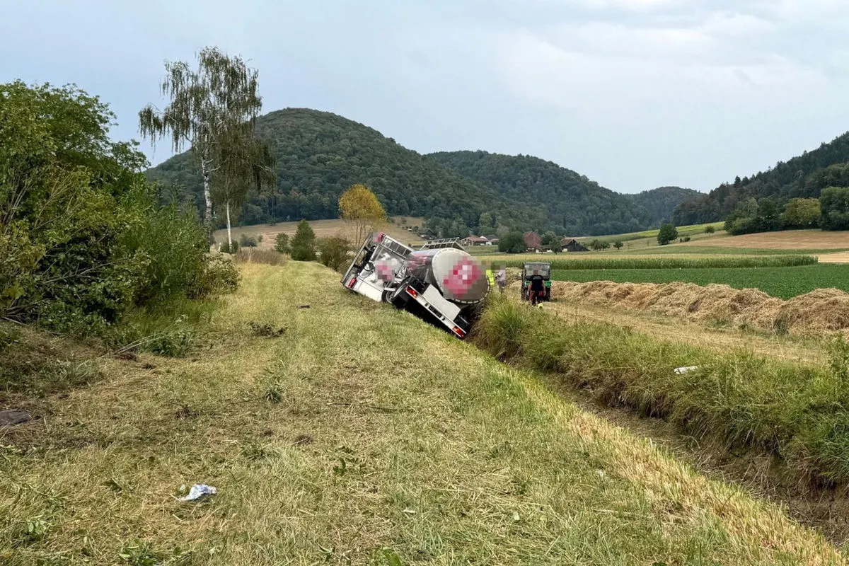 Ein Lastwagen ist auf einem ländlichen Weg in einen Graben gekippt. Im Hintergrund sind Felder und Hügel zu sehen.