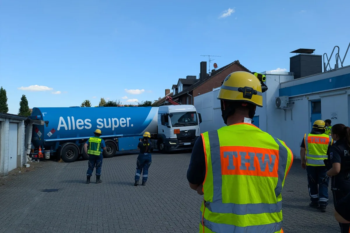 Ein blauer Tanklaster mit der Aufschrift 'Alles super.' steht vor einer beschädigten Garage, während THW-Kräfte die Lage sichern.
